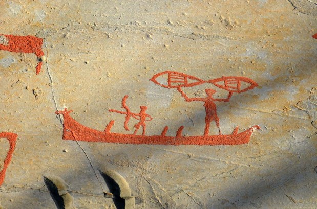 Hunting with bow and arrow from a skin boat with its prow formed as the head of an elk. The human with raised arms is probably holding a pair of snow shoes. Photo: Per Storemyr