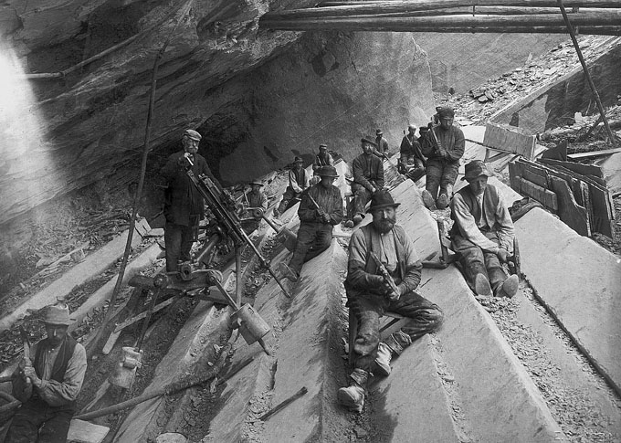 Fra skiferbruddet ved Skarsjøen, et av de mange bruddene som var i drift i Stjørdal fra midten av 1800-tallet og utover. Steinbryterne hogger lange kanaler på tvers av kløven i skiferen, som så blir kilt ut som plater. En tidlig boremaskin har kommet på plass, men akkurat her er den satt opp kun for å vises frem. Ukjent fotograf, ca. 1900. Fra Pettersson 1999.