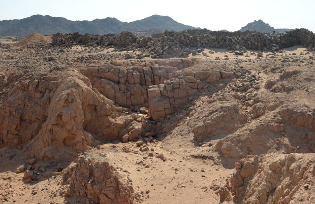 Part of the granite bedrock of the amethyst mine at site 9 in Wadi el-Hudi. The granite has been subject to deep weathering over millions of years. In the background the fortified settlement that was partially built with weathered rock from the mine. Photo by Per Storemyr