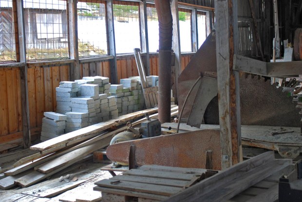 I saghuset på Sagflaten: Sirkelsag, rustet avsug og i bakgrunnen et forlatt lager med kleber som var ment for ildfaststein. Foto: Per Storemyr (2018)