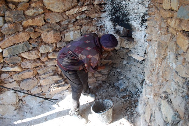 Ekstra tetting av murverket rundt åpningen med kalkmørtel etter ca. ett døgns brenning. Legg merke til jernstanga med gaffel som brukes til å rette opp veden i ovnen.