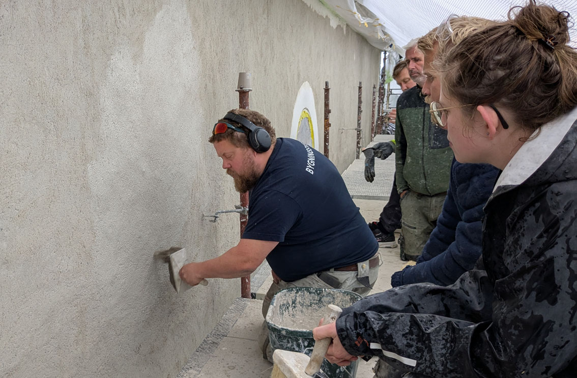 Tore Granmo instruerer ved murerkurs på Tanum kirke sommeren 2026. Alt arbeid på veggen er ved kursdeltakerne - og kalken er fra ovnene i Tvedestrand. Foto: PS 
