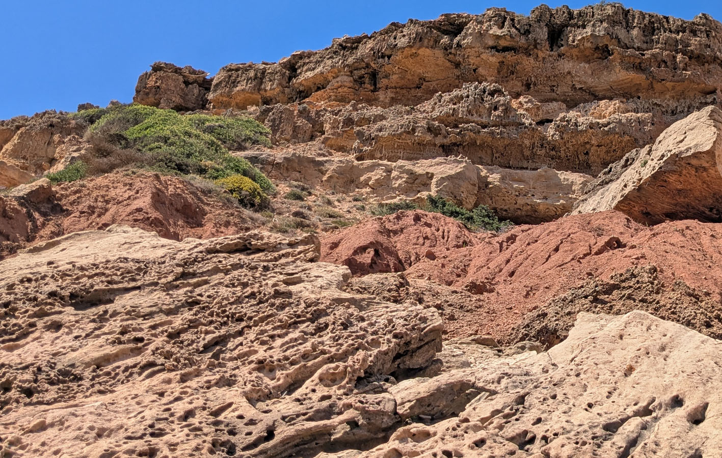 Differential weathering related to rhizoliths and tafoni has undermined the young, Quaternary calcareous sandstone at the top, contributing to rock fall at Telheiro beach. Tafoni on fallen blocks in the foreground. Photo by PS